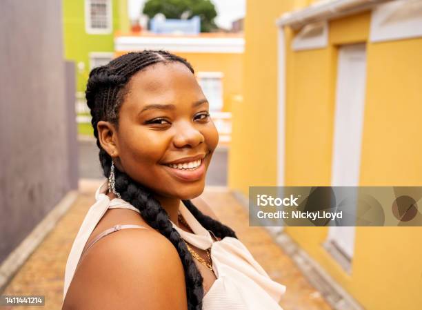Smiling Young Woman Walking Down An Alley With Colorful Buildings Stock Photo - Download Image Now