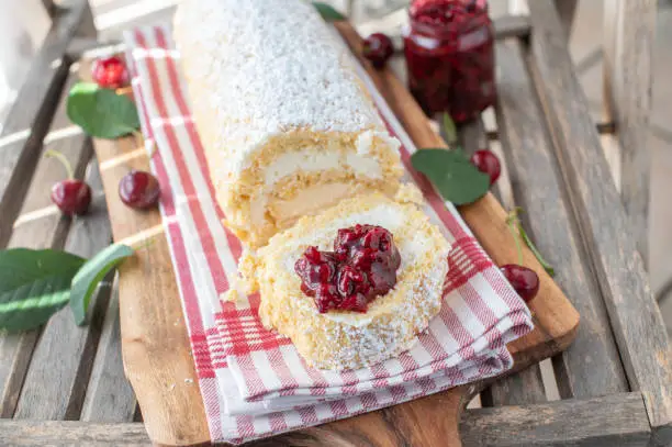 Traditional fresh and homemade baked swiss roll filled with whipped cream and topped with sour cherry compote