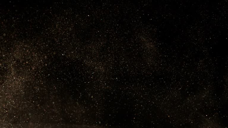 Super slow motion of glittering golden particles on black background.