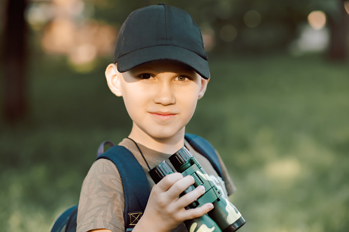 Little boy scout with backpack and binoculars during hiking in forest. Concepts of adventure, journey, scouting and hiking tourism for kids