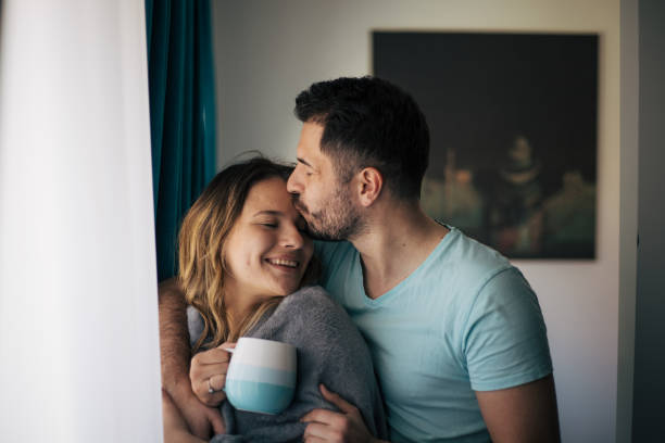 Young heterosexual couple standing behind the window and smiling stock photo