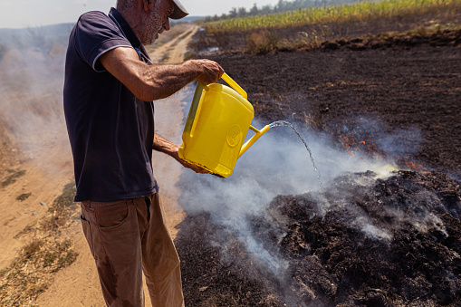 Cut out shot of man pouring water on burned stubble in the field and extinguishing the fire set deliberately