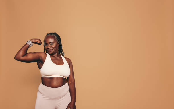 mujer madura flexionando su bíceps en un estudio - musculoso fotografías e imágenes de stock