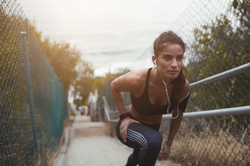 Athletic young woman doing stretch exercises on a staircase outdoors. Sporty young woman warming up before going out for a run in the morning.