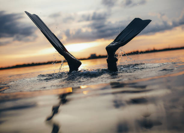 Scuba diver diving into the sea with his fins above the water. Man scuba diving at sunset.