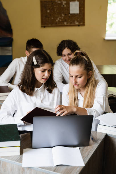 istock Back to school. Children reading book at geography lesson and discuss different countries with globe. Pupils at school study online on laptop and communicating with classmates online. 1411451326