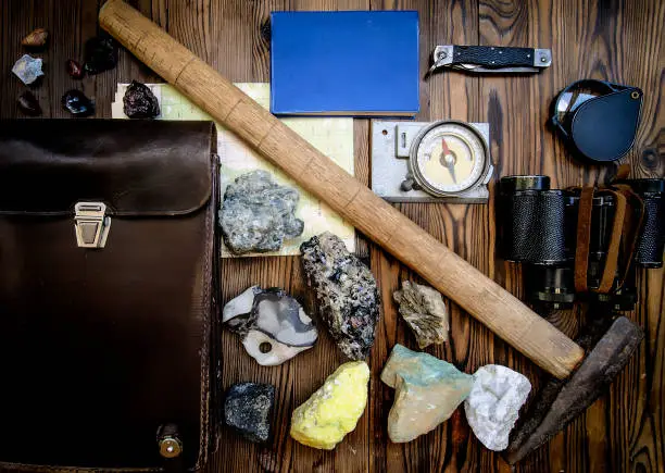 Geological fieldwork tools: map case, geological hammer, compass, magnifying glass, pocket knife, binoculars, drill core, rock samples, topographic map