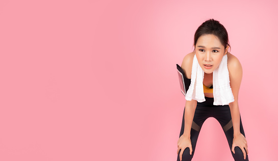 Tired fitness girl get exhausted and fatigue after exercise or workout Sport woman bend down and hands on knees with disheartened Pretty young Asian woman take a break after running Isolated on pink