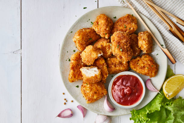 Chicken nuggets in a plate, with ketchup, salad and lemon, served on a white wooden table Chicken nuggets in a plate, with ketchup, salad and lemon, served on a white wooden restaurant or home table, top view with copy space nugget photos stock pictures, royalty-free photos & images
