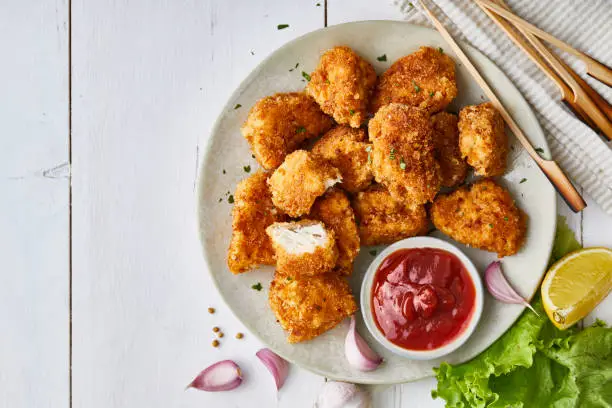 Photo of Chicken nuggets in a plate, with ketchup, salad and lemon, served on a white wooden table