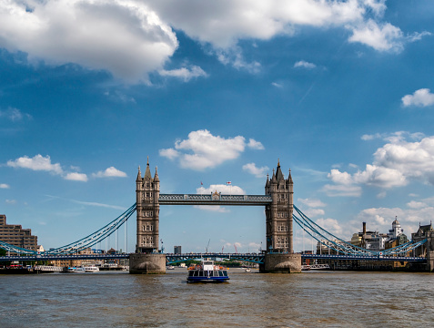 Tower Bridge in London, seen from the River Thames and whilst travelling downstream towards the Thames Estuary. A tourboat is approaching the bridge.