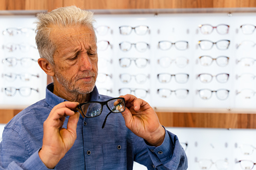 senior man trying on eyeglasses in front of mirror at optician store