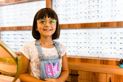 smiling girl customer selecting spectacles in optical store