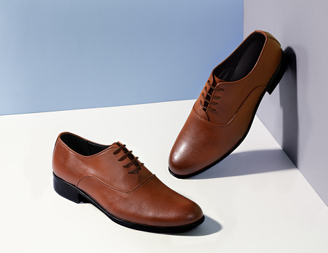 A pair of classic styled, brown colored, leather male shoes on a white and blight blue background