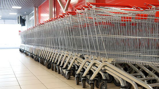 Many steel shopping trolleys with red handles standing in a row