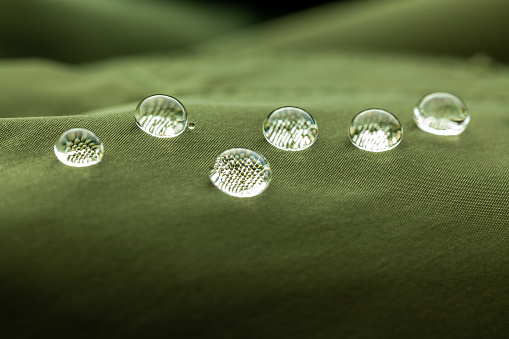 Extreme closeup of beautiful water droplets on dark green waterproof fabric
