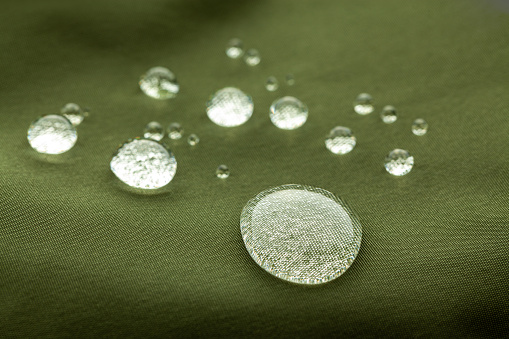 Extreme closeup of beautiful water droplets on dark green waterproof fabric