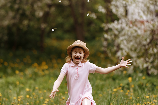 Girl in a hat and a pink dress runs across a field with dandelions