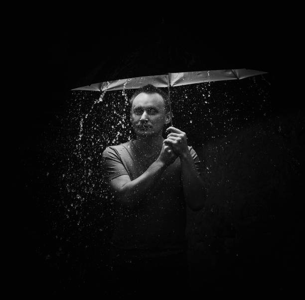 istock young man standing under umbrella on dark background. It's raining. Light on male 1411476432