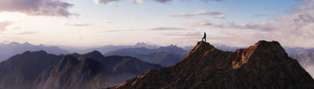 abenteuerlustiger menschenwanderer auf einem felsigen berg stehend mit blick auf die dramatische landschaft - berggipfel stock-fotos und bilder