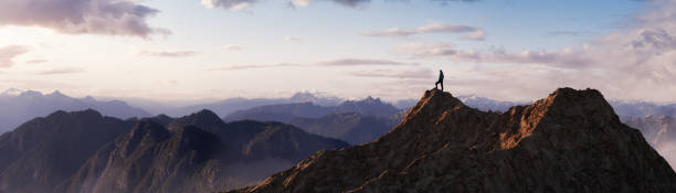 avventuroso uomo escursionista in piedi sulla cima di una montagna rocciosa che domina il paesaggio drammatico - vetta foto e immagini stock