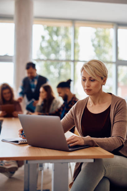 istock Mid adult woman taking notes while e-learning on laptop in the classroom. 1411477886
