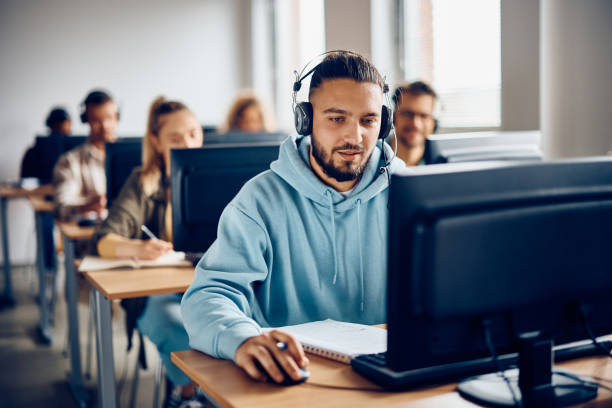 Young student e-learning on a computer at university classroom. Male student using desktop PC during computer class at the university. computer lab stock pictures, royalty-free photos & images