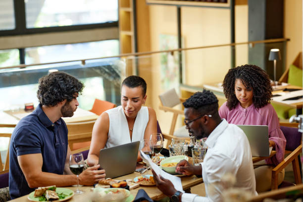 A group of casual businesspeople is sitting in a restaurant for a meeting, discussing a project while having dinner. stock photo