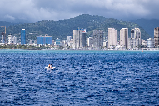 Honolulu, HI - May 3, 2022: Coastline of Waikiki with two people in an inflatable raft far from the beach.