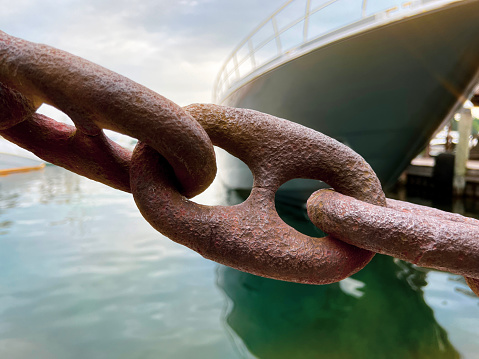 Rusty iron nautical-style chains linked together to form a barrier in front of an enormous yacht. Focus on foreground, with blurred background. Located in a harbor on Lake Michigan.