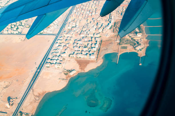 Beautiful nature scene on the land with ocean through airplane window. Airplane wing and view from the airplane Window over the ocean or sea area with desert sand land and cities. Look from above through plane window during the flight