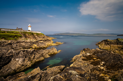 rocky shoreline with turquoise pools and the historic Broadhaven Lighthouse on a clifftop promontory at the entrance of Broadhaven Bay