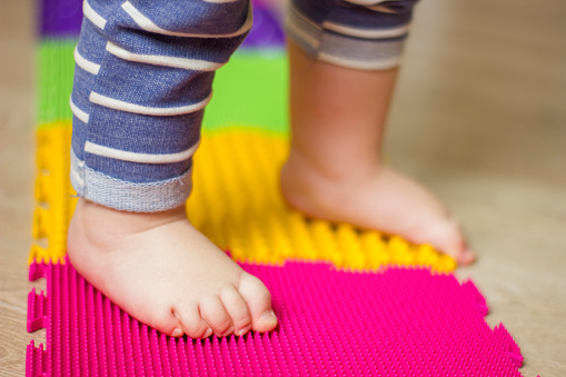 Closeup toddler baby's feet on orthopedic massage mat. Baby foot massage. Exercises for legs on carpet. Orthopedic massage puzzle floor mats for development of children. Focus picked.