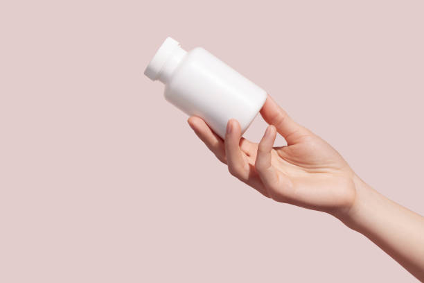istock Female hand holding blank white squeeze bottle plastic tube on pink background. Packaging for pills, capsules or supplements. Mockup. 1411483319