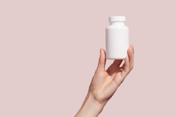 ピンクの背景に空白の白いスクイーズボトルのプラスチックチューブを保持している若い女性の手。モックアップ。 - capsule pill white nutritional supplement ストックフォトと画像