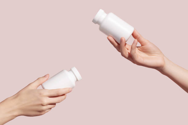 istock Hands holding blank white plastic tubes on pink background. Packaging for pills, capsules or supplements. Medic product branding mockup. 1411483327