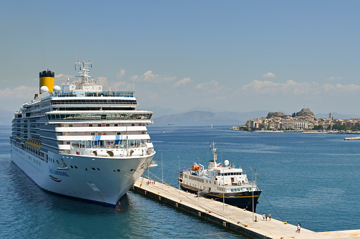 Corfu, Greece - June 2022: Costa Luminosa cruise ship and small passenger ferry moored in the port of Corfu town with the town and harbour in the background