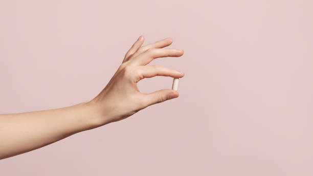 ピンクの背景にサプリメントを保持する手 - vitamin capsule 写真 ストックフォトと画像