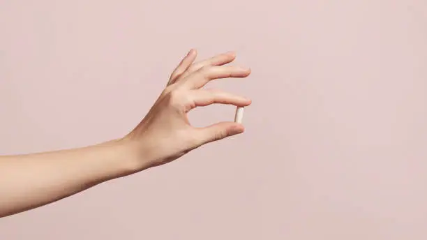 Photo of Hand holding the supplements on pink background