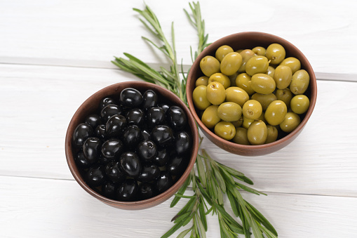 Black and green olives on a white wooden background.
