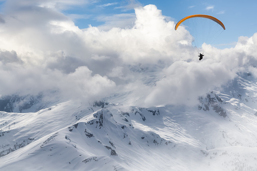 Adventure Composite Image of Paraglider Flying up high in the Rocky Mountains. Cloudy Sky. Aerial Background from British Columbia, Canada. Extreme Sport Concept. winter