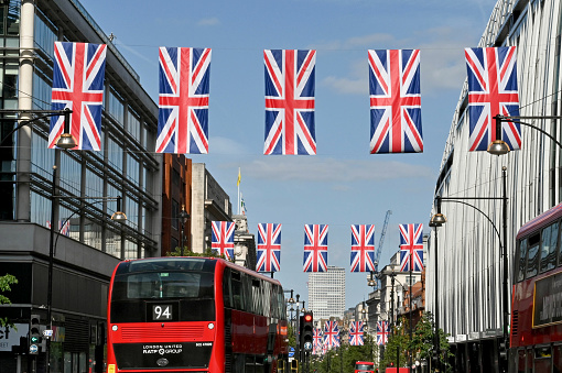 London, England - June 2022: Rows of Union Jack flags hanging over Oxford Street, with red London buses driving along the road