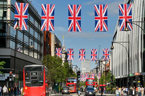 London, England - June 2022: Rows of Union Jack flags hanging over Oxford Street, with red London buses driving along the road