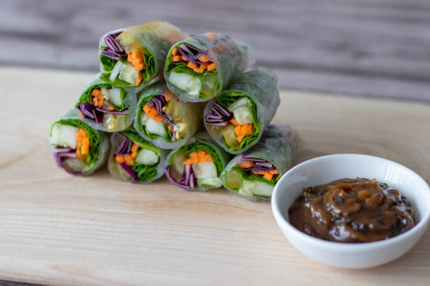 istock Vegan vegetable spring rolls in rice paper on a board with peanut paste, soy sauce and black sesame sauce. 1411484966