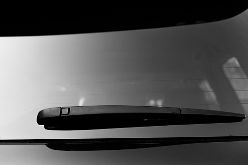 close up of back wiper on black new car windows. A windscreen wiper or windshield wiper is a device used to remove rain, snow, ice and debris from a windscreen or windshield