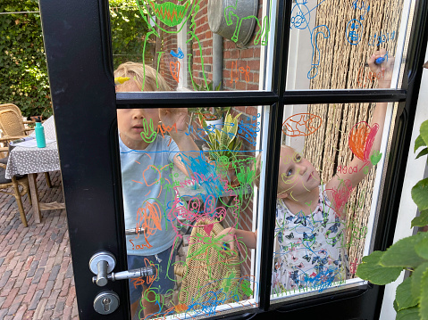Brother and sister children maken a window paint on the kitchen door.