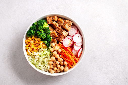 Vegan buddha bowl with tofu, colorful vegetables on base of brown rice. Top view, healthy vegetarian bowl dish on white table, top view, copy space