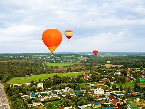 Large beautiful hot balloons fly high in the sky over scenery green field and forest. Extreme entertainment for vacation and leisure.