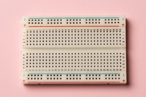 An electronics breadboard on pink background.