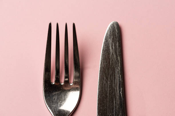 Metal fork and knife on a pink table..